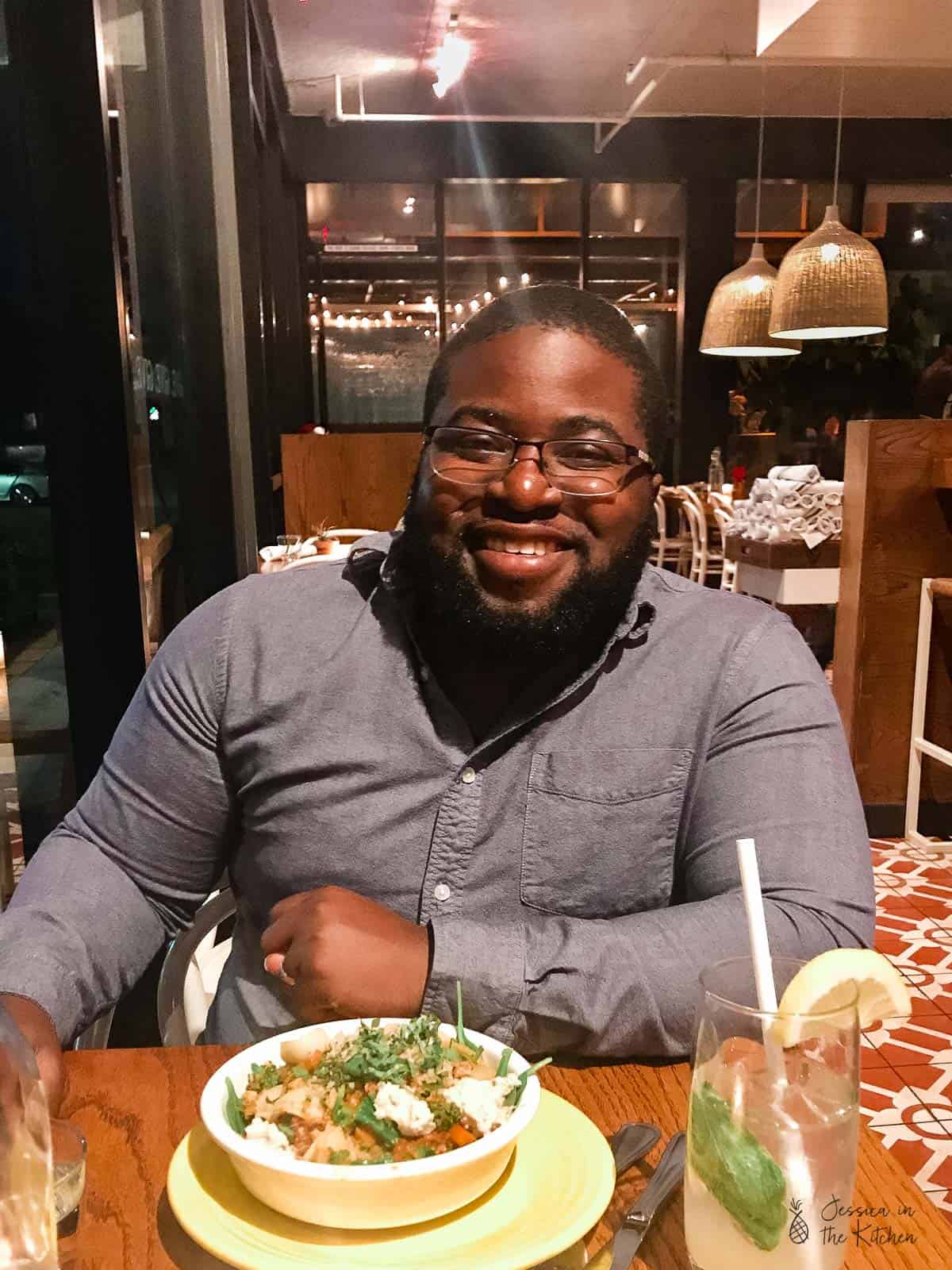 Gavin in a grey shirt, sat in a restaurant, smiling to camera. 