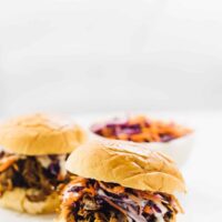 Side on shot of two vegan pulled pork sandwiches on a white plate, with slaw in the background.