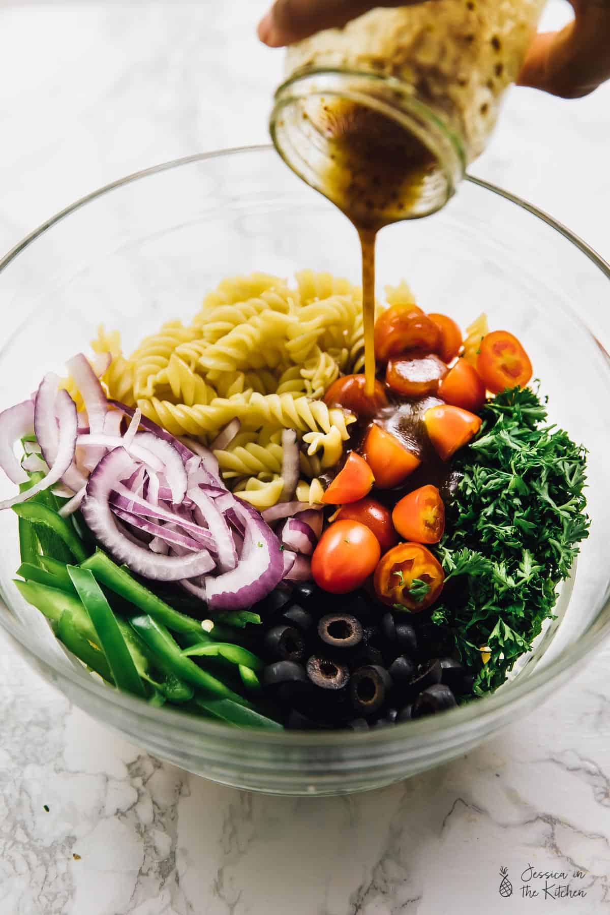 Pouring dressing on vegan pasta salad in a glass bowl. 