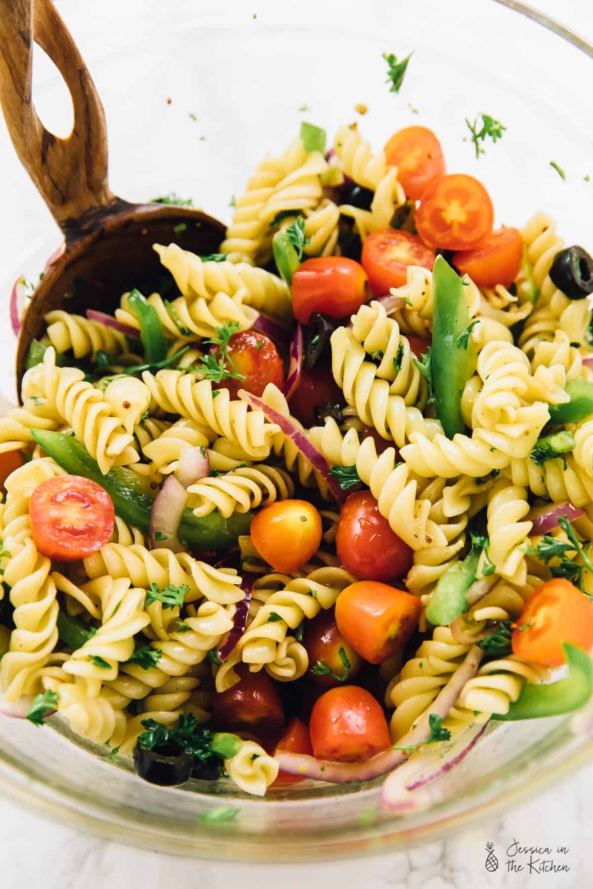 Stirring vegan pasta salad in a glass bowl. 