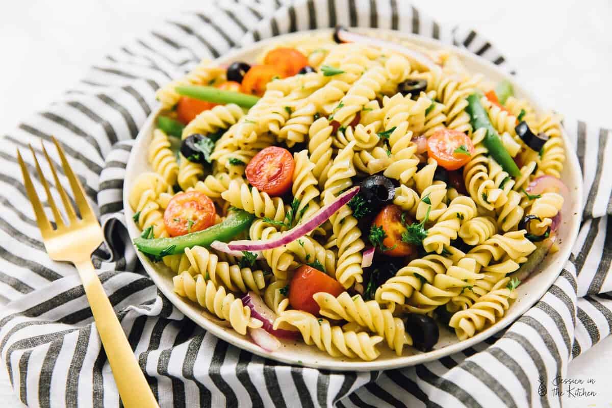 Vegan pasta salad on a plate with a golden fork on the side. 
