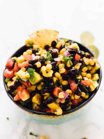 Black bean avocado and corn salad in a white bowl with a chip dipped in it.