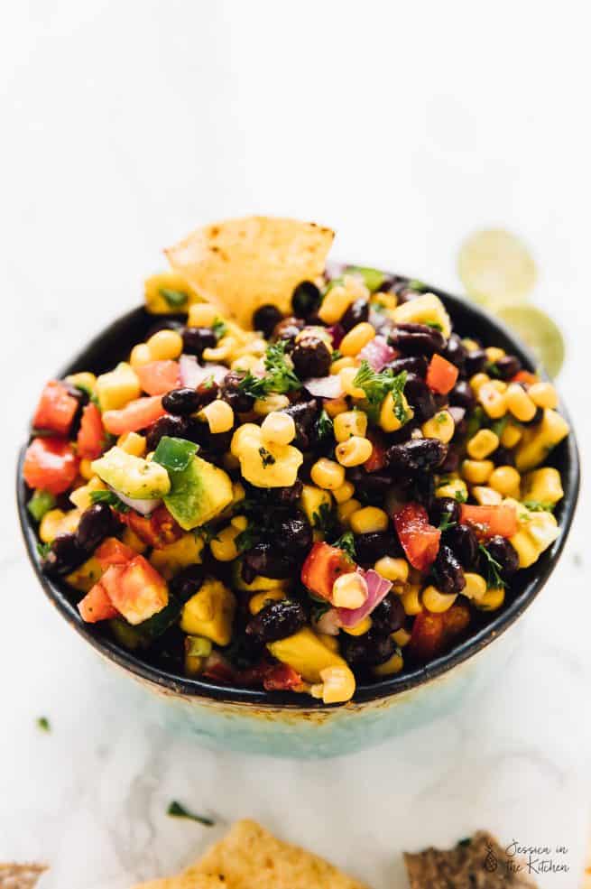 Black bean avocado and corn salad in a white bowl with a chip dipped in it.