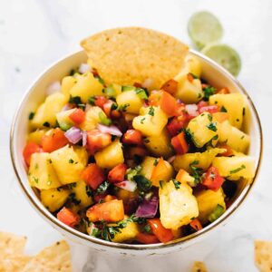 A bowl of pineapple salsa with a tortilla chip dipped in.