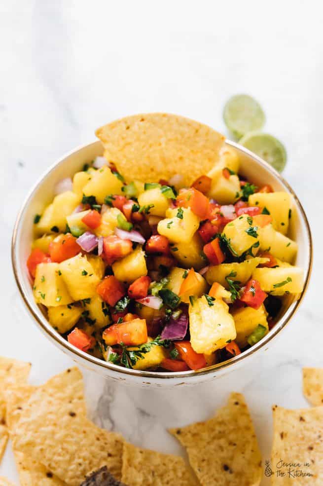 A bowl of pineapple salsa with a tortilla chip dipped in.