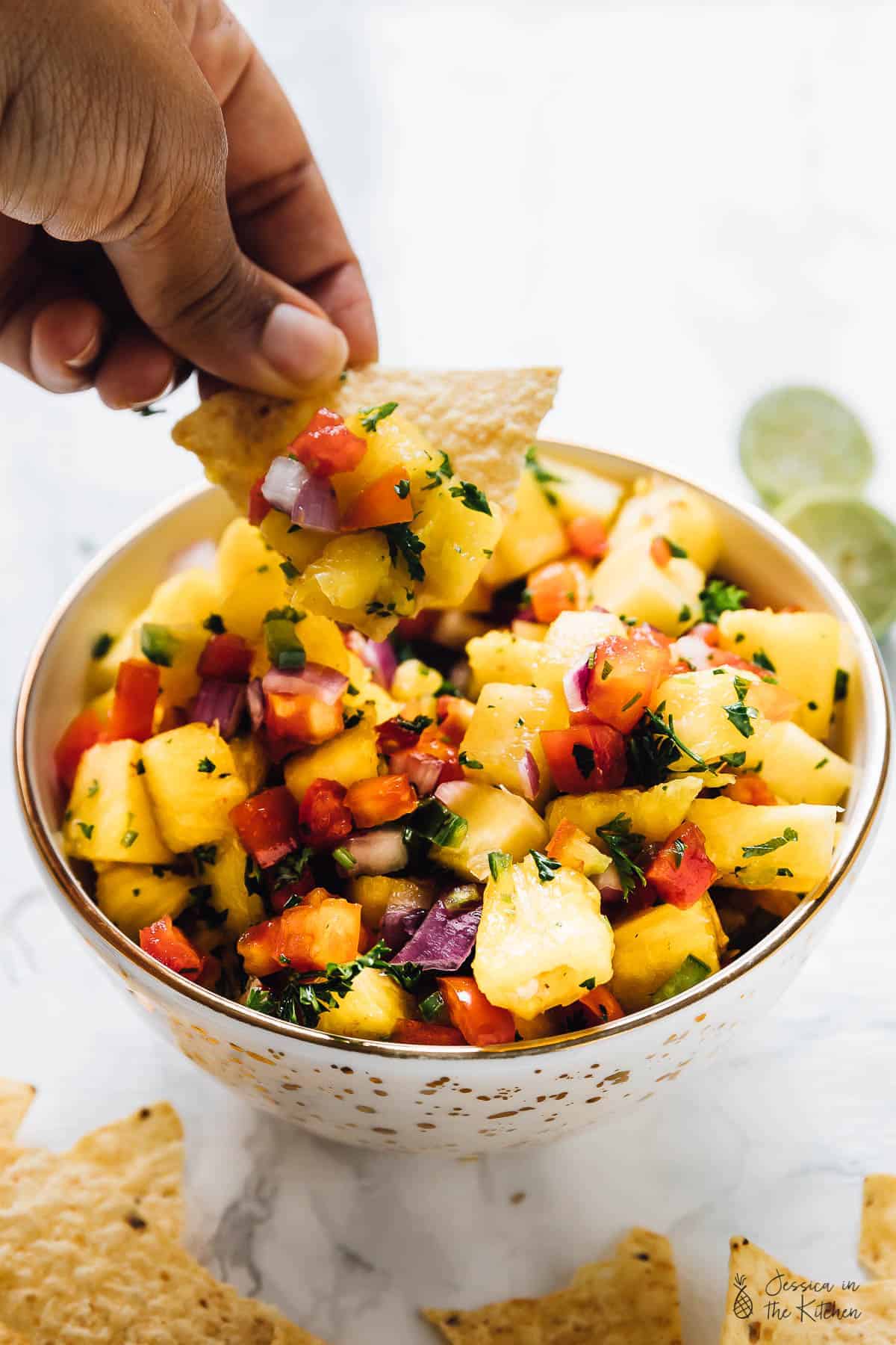 Hand dipping a chip into a bowl of pineapple salsa.