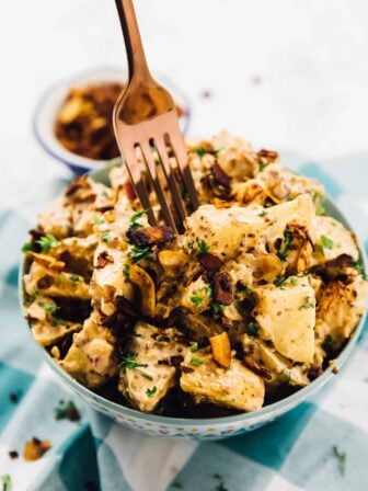 A fork sticking into a bowl of loaded vegan potato salad with coconut bacon.