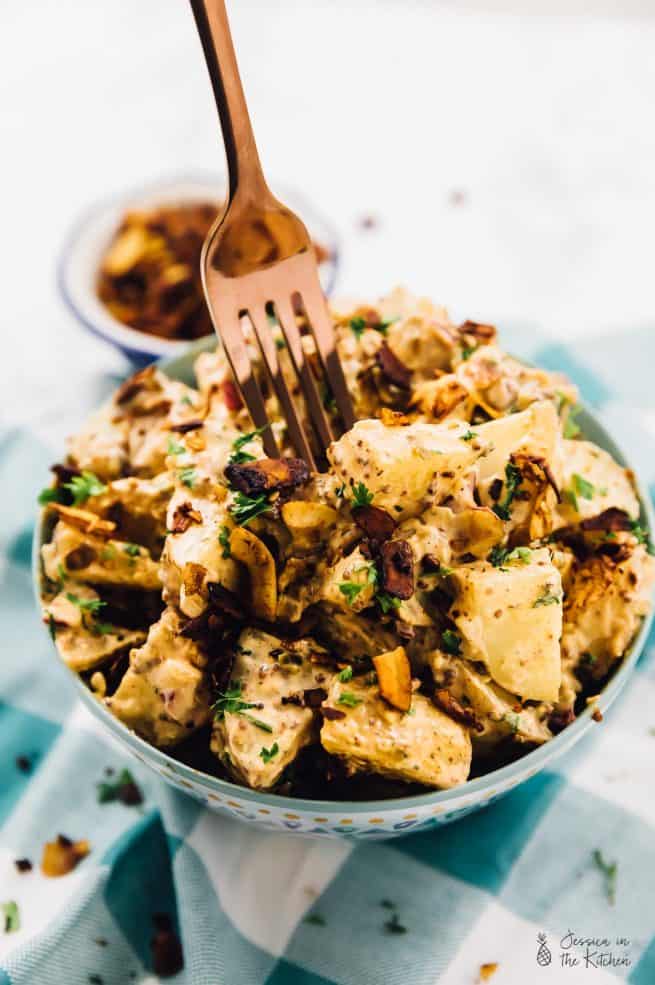 A fork sticking into a bowl of loaded vegan potato salad with coconut bacon.