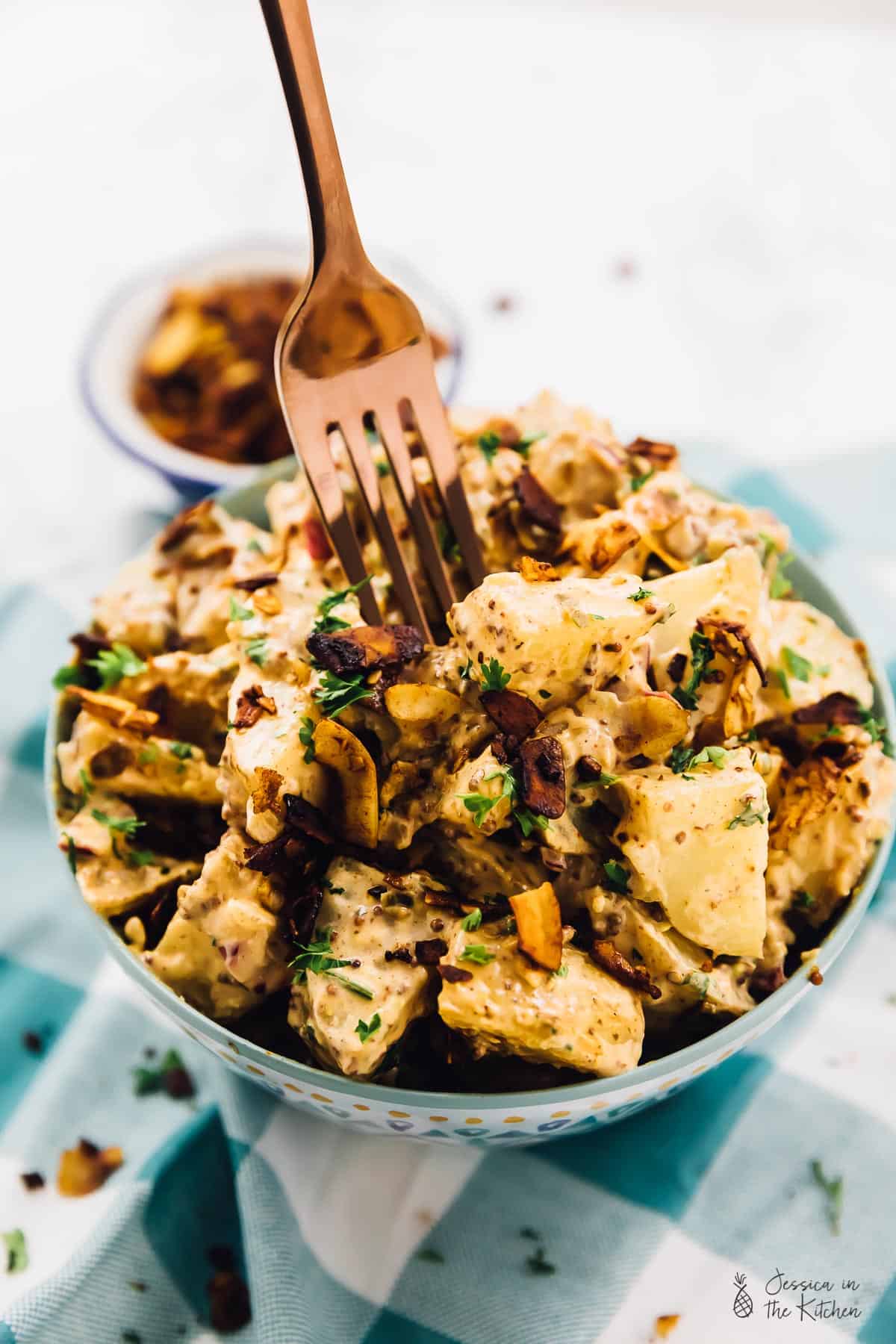 A fork digging into a bowl of loaded vegan potato salad. 