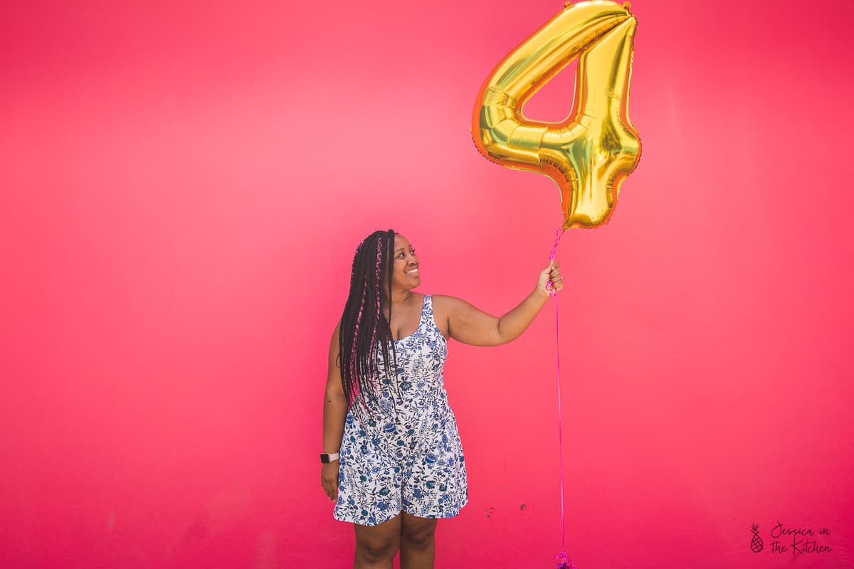 Jessica holding up a four balloon against a pink backdrop. 