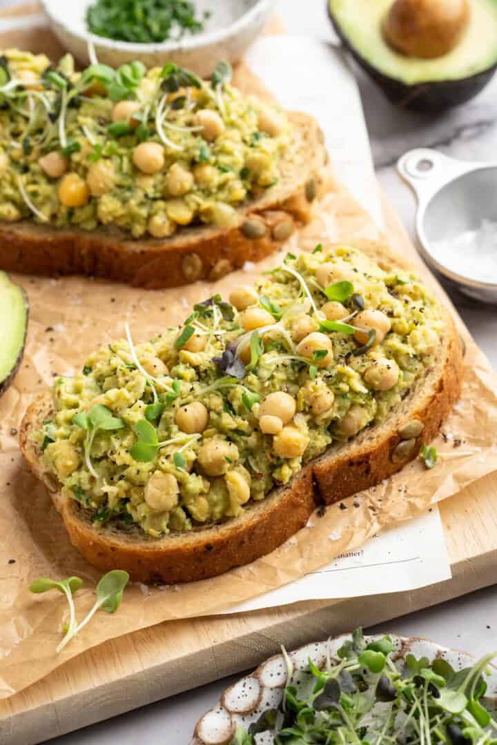 Two slices of bread topped with smashed chickpea avocado salad and microgreens
