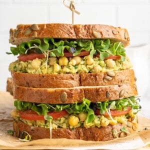 Two smashed chickpea avocado salad sandwiches stacked on cutting board