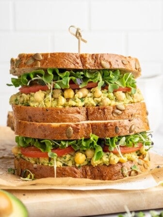 Two smashed chickpea avocado salad sandwiches stacked on cutting board