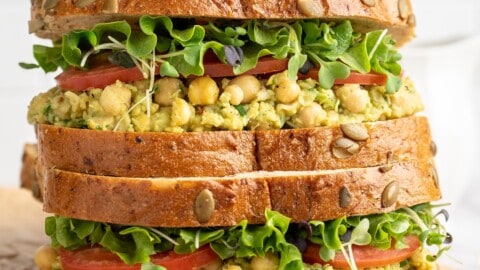 Two smashed chickpea avocado salad sandwiches stacked on cutting board