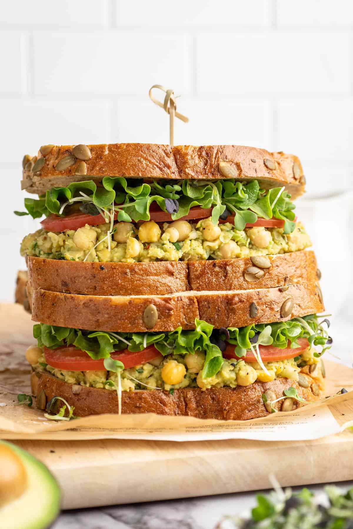 Your meal prep lunches just got easier AND tastier thanks to this Smashed Chickpea Avocado Salad Sandwich recipe. The perfect vegan lunch! Two smashed chickpea avocado salad sandwiches stacked on cutting board