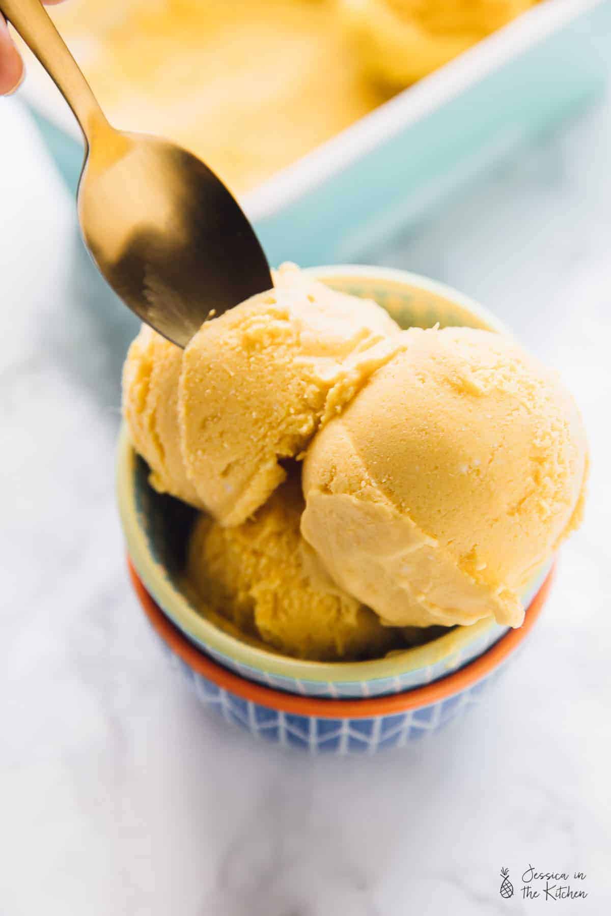 Spoon digging into scoops of vegan mango ice cream in bowl