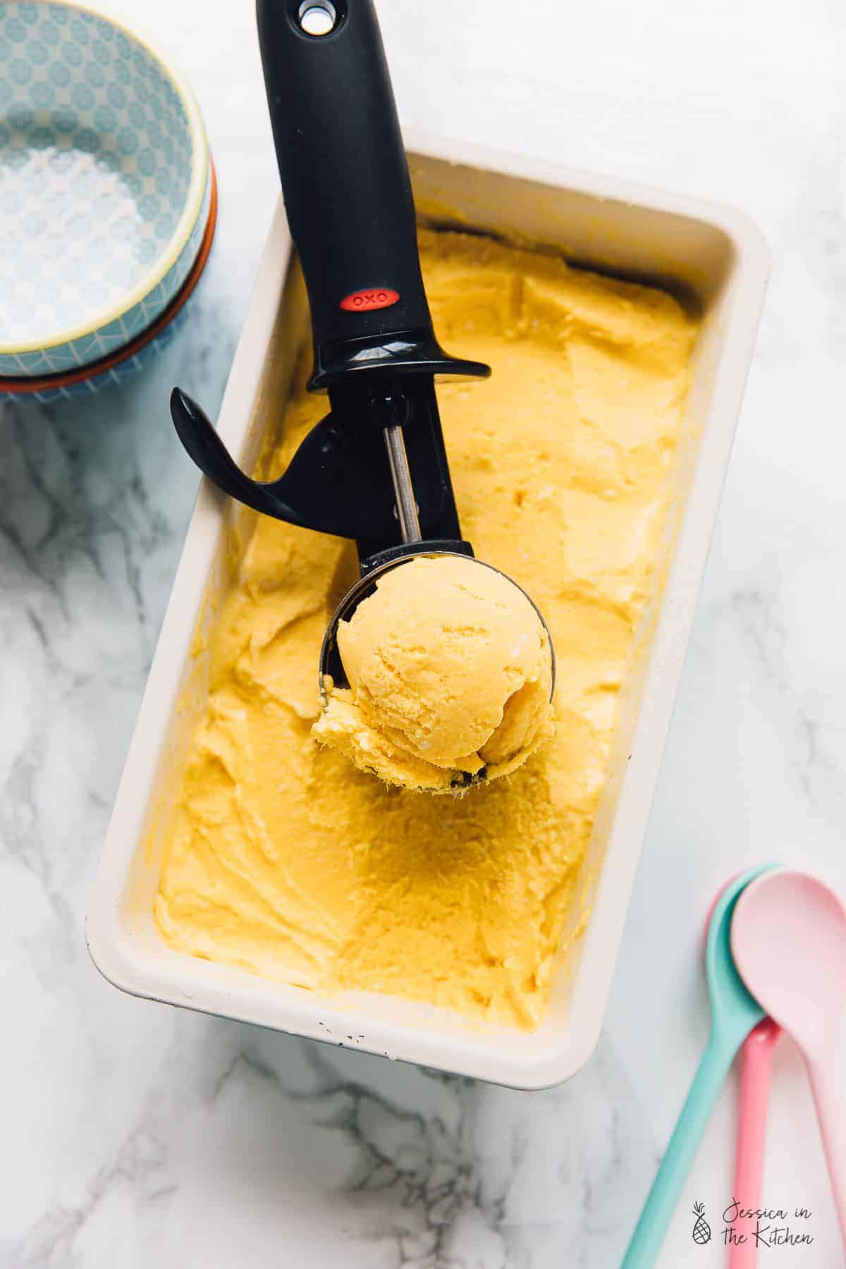 Vegan mango ice cream in a white tub with a scoop on top. 