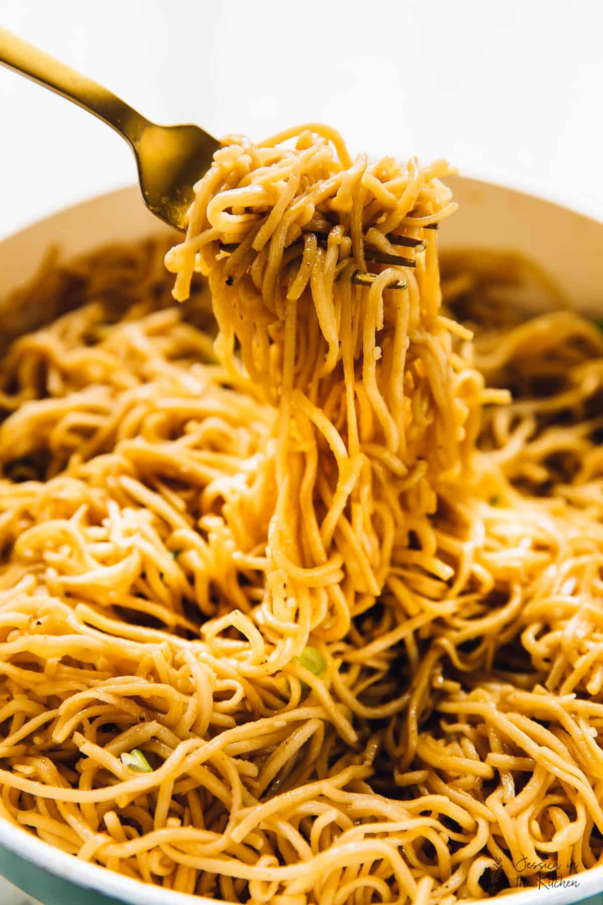 A fork pulling up sesame noodles form a bowl. 