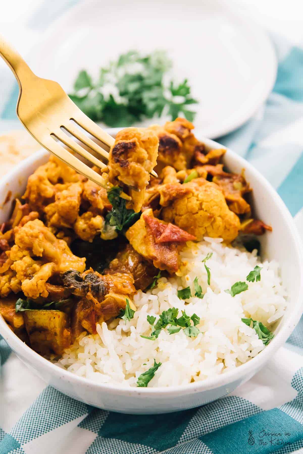 A fork digging into cauliflower and potato curry with rice on the side. 