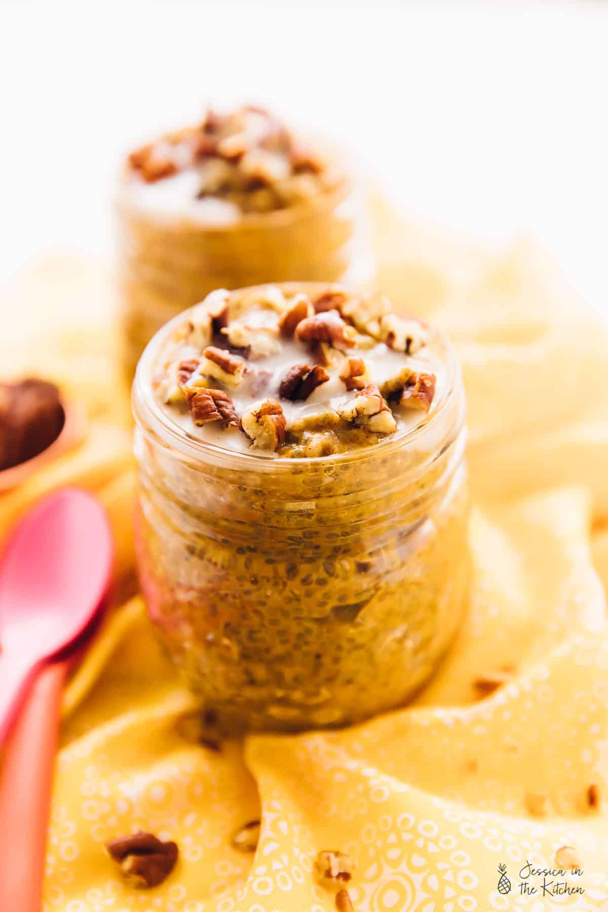 A jar of chia pudding topped with pecans, with another jar and a spoon in the background