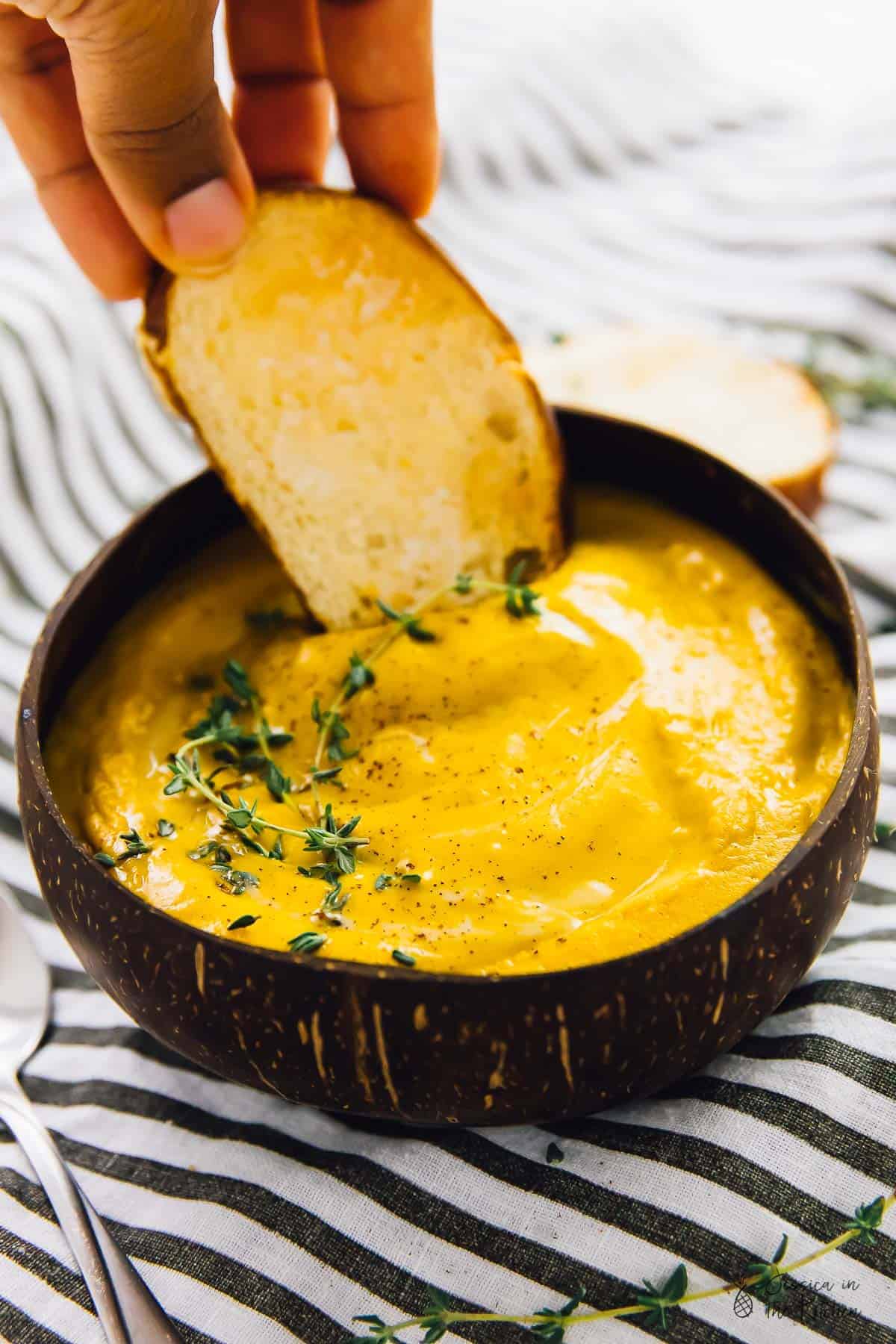 Hand dipping bread into a bowl of soup.