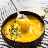 A spoon being dipped into a bowl of roasted sweet potato soup.