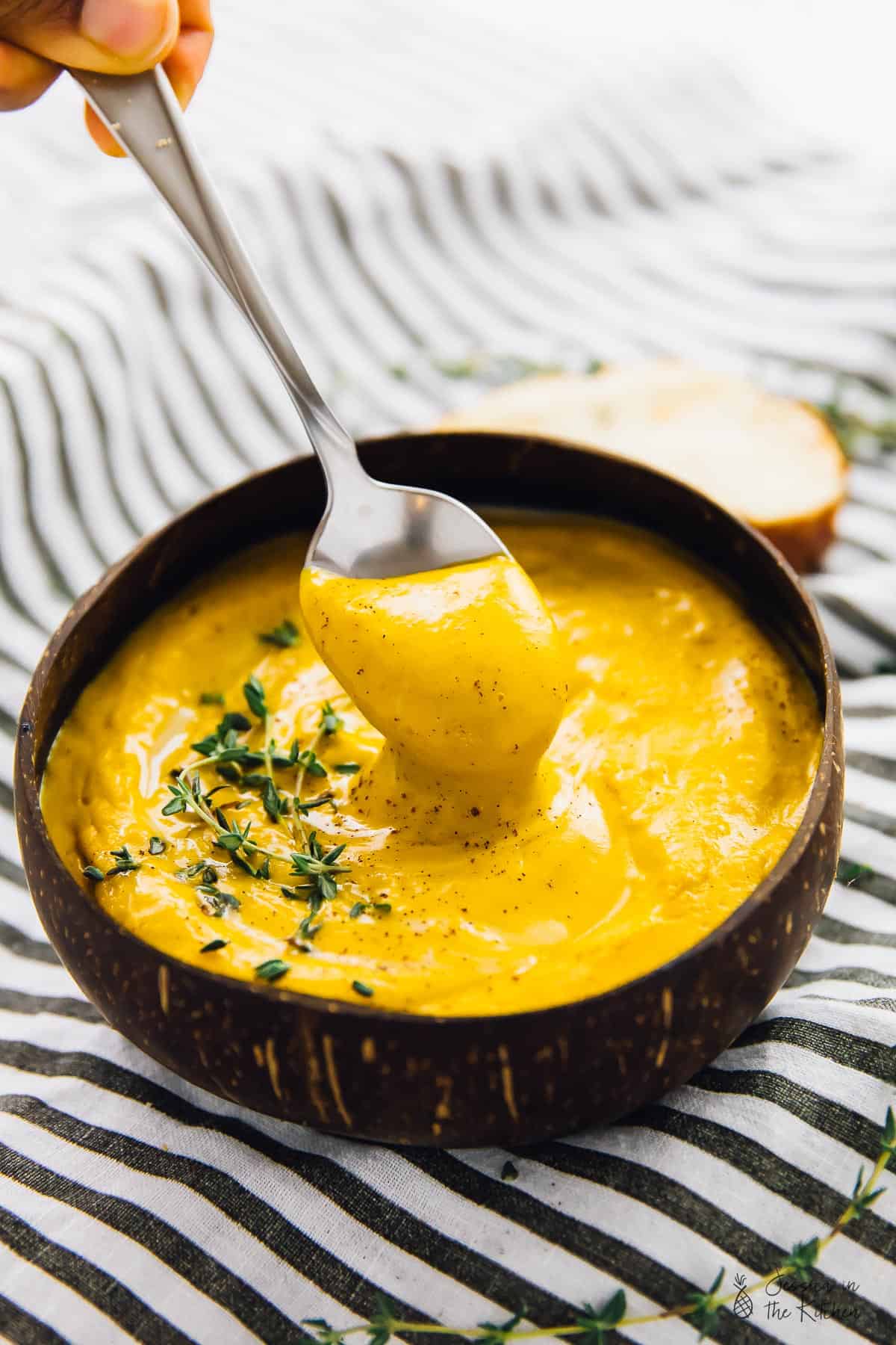 A spoon dipped into a bowl of roast sweet potato soup. 