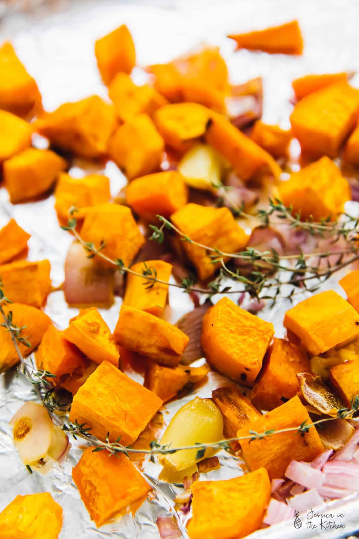 Roasted sweet potato on a baking sheet with thyme and onions and garlic.