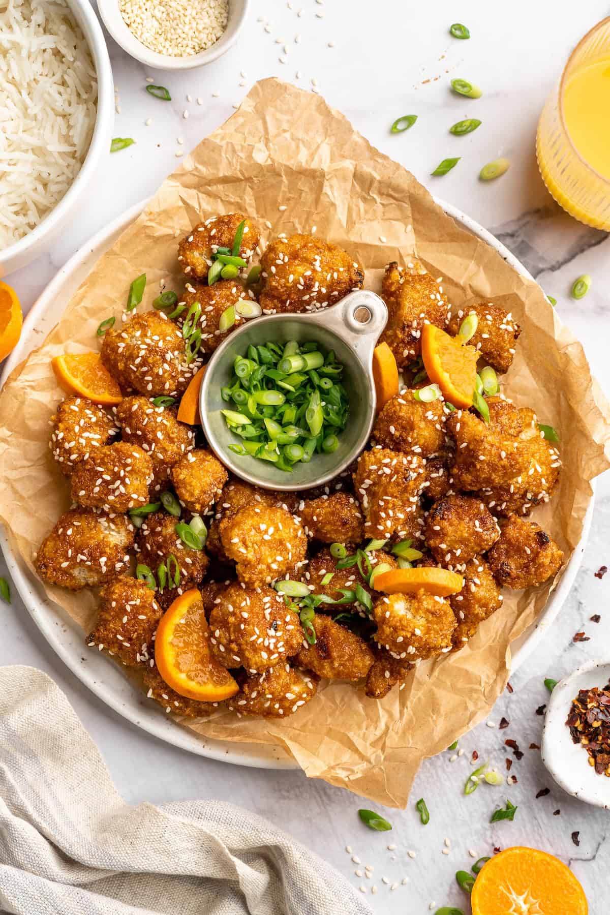 Overhead view of crispy orange cauliflower on platter with bowl of scallions