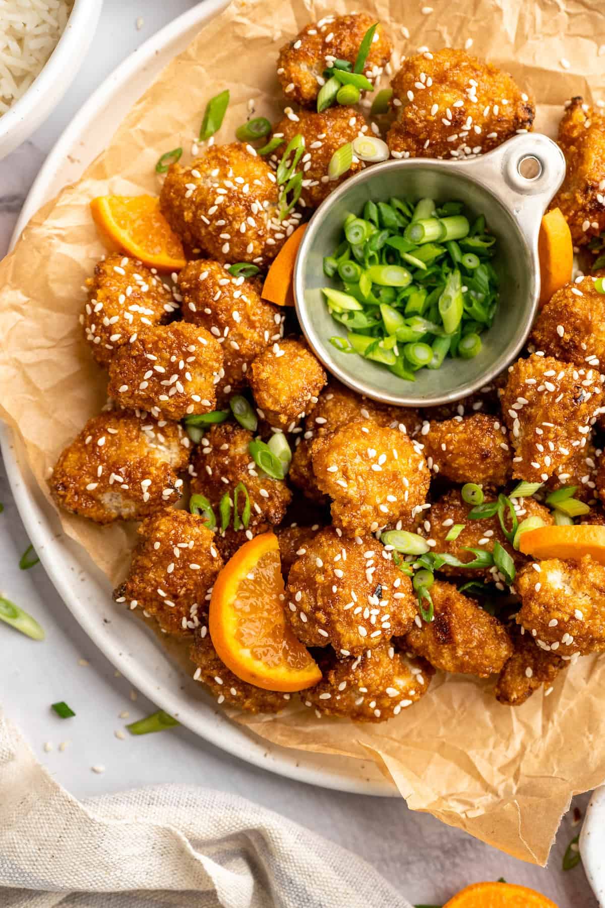 Overhead view of crispy orange cauliflower with bowl of scallions