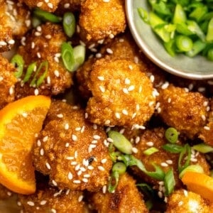 Overhead view of crispy orange cauliflower with bowl of scallions