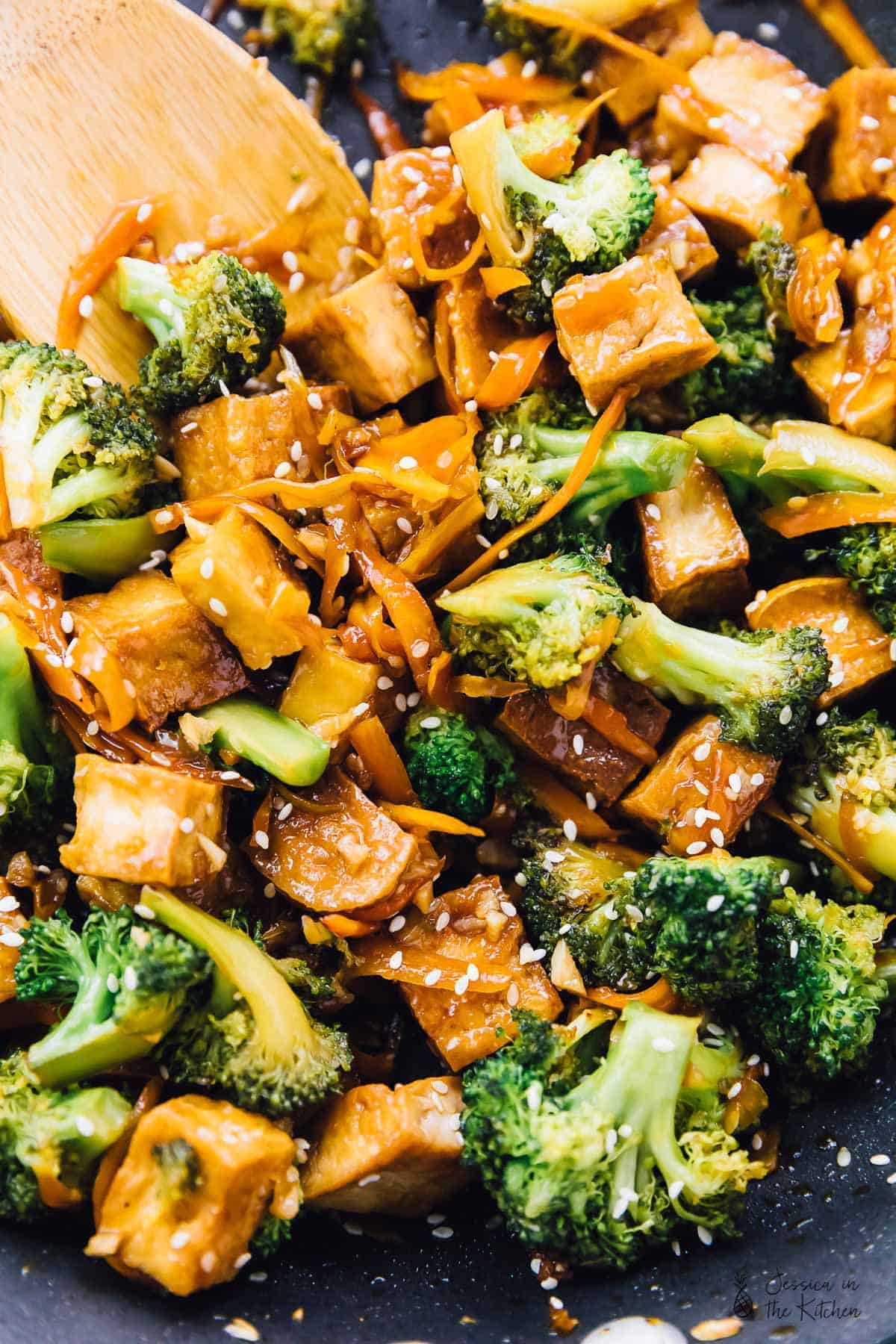 A wooden spoon stirring tofu and veggie stir fry in a skillet. 