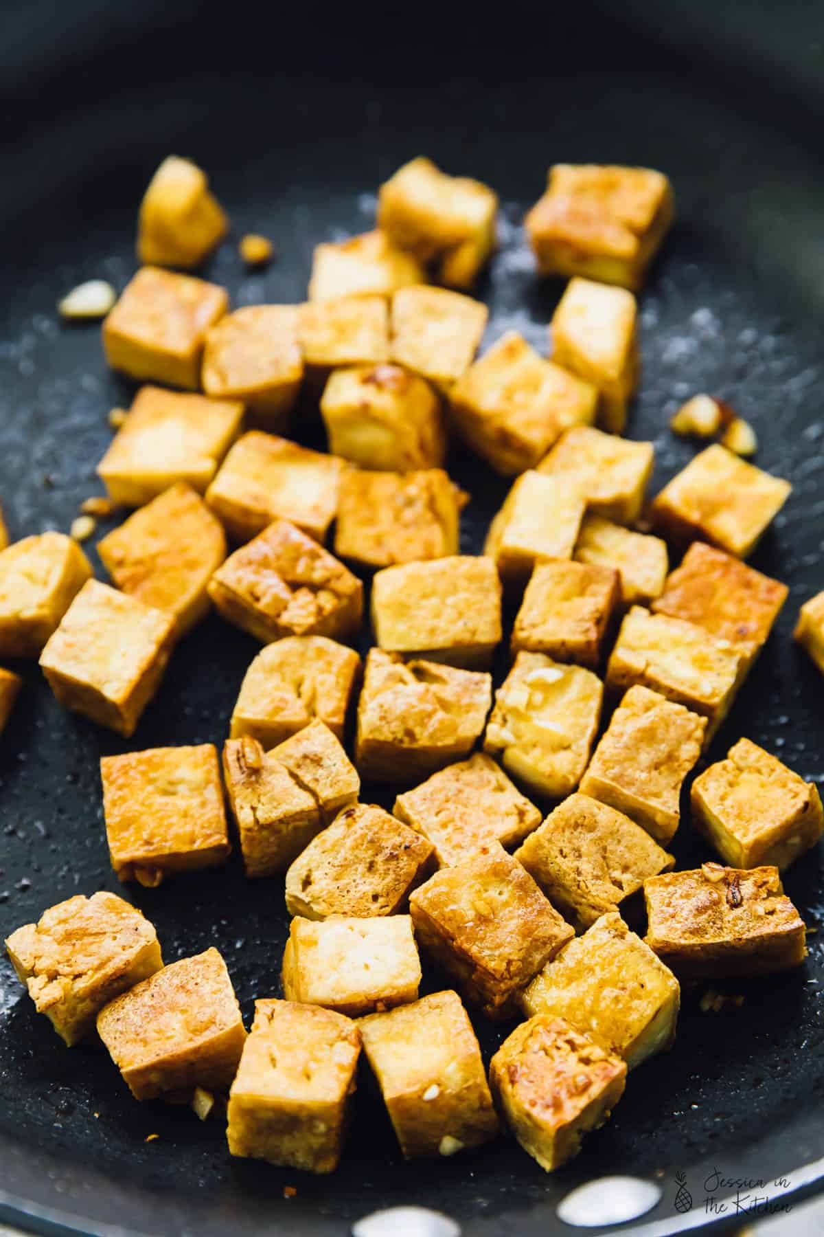 Tofu cooking in a black skillet. 