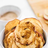 Cinnamon apple chips in a bowl, with sauce in the background.