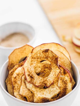 Cinnamon apple chips in a bowl, with sauce in the background.