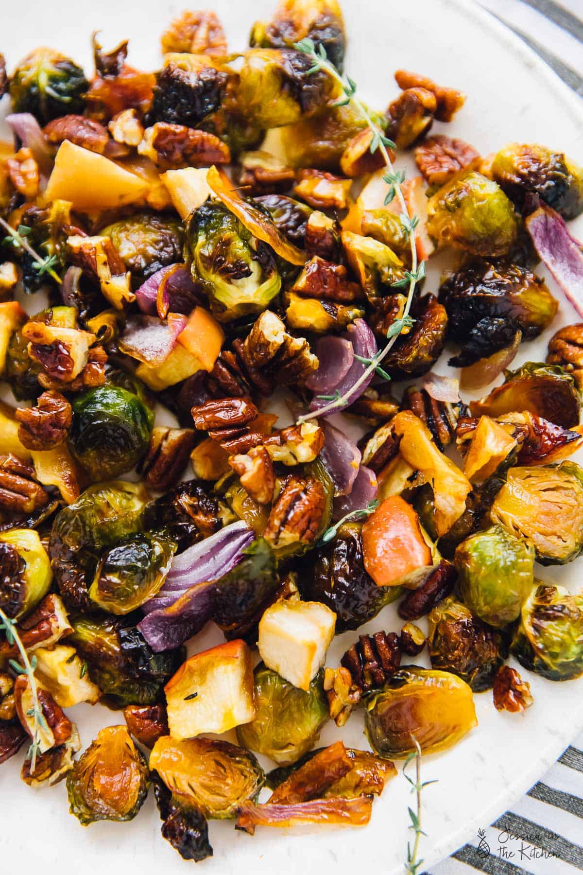 Overhead view of roasted Brussels sprouts, onions, and apples, with thyme and pecans. 