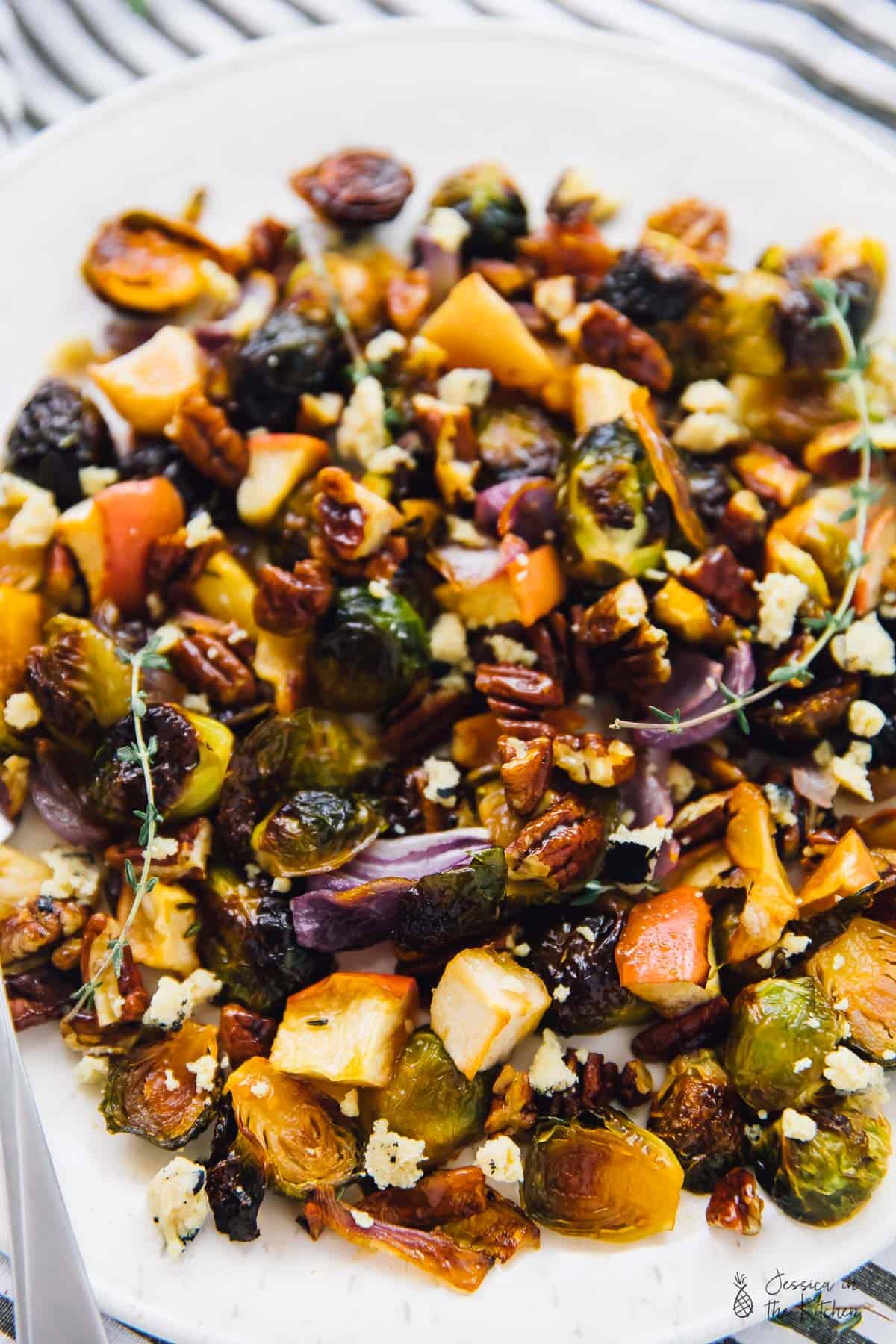 A plate of roasted Brussels sprouts, apples, onions, and thyme, topped with pecans and vegan cheese. 