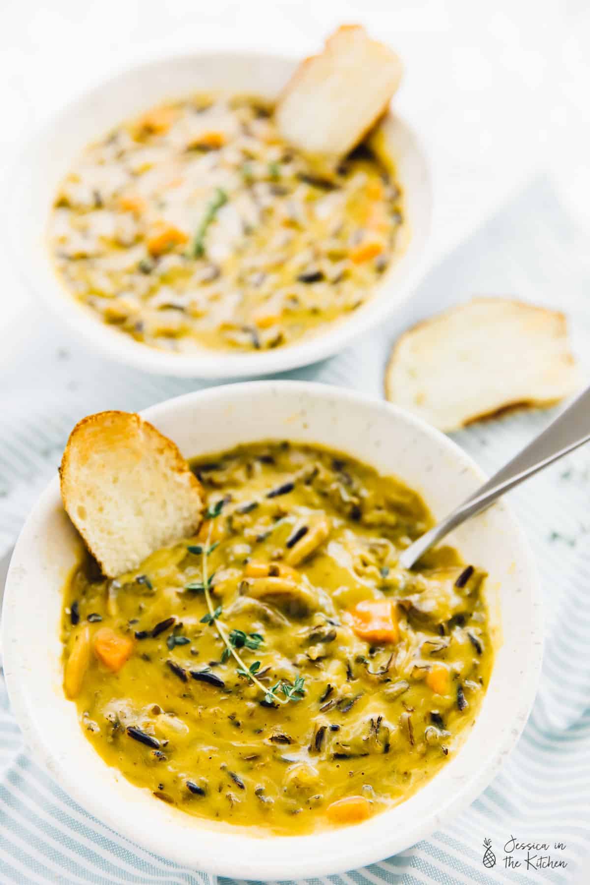 A bowl of mushroom wild rice soup with a slice of bread dunked in. 