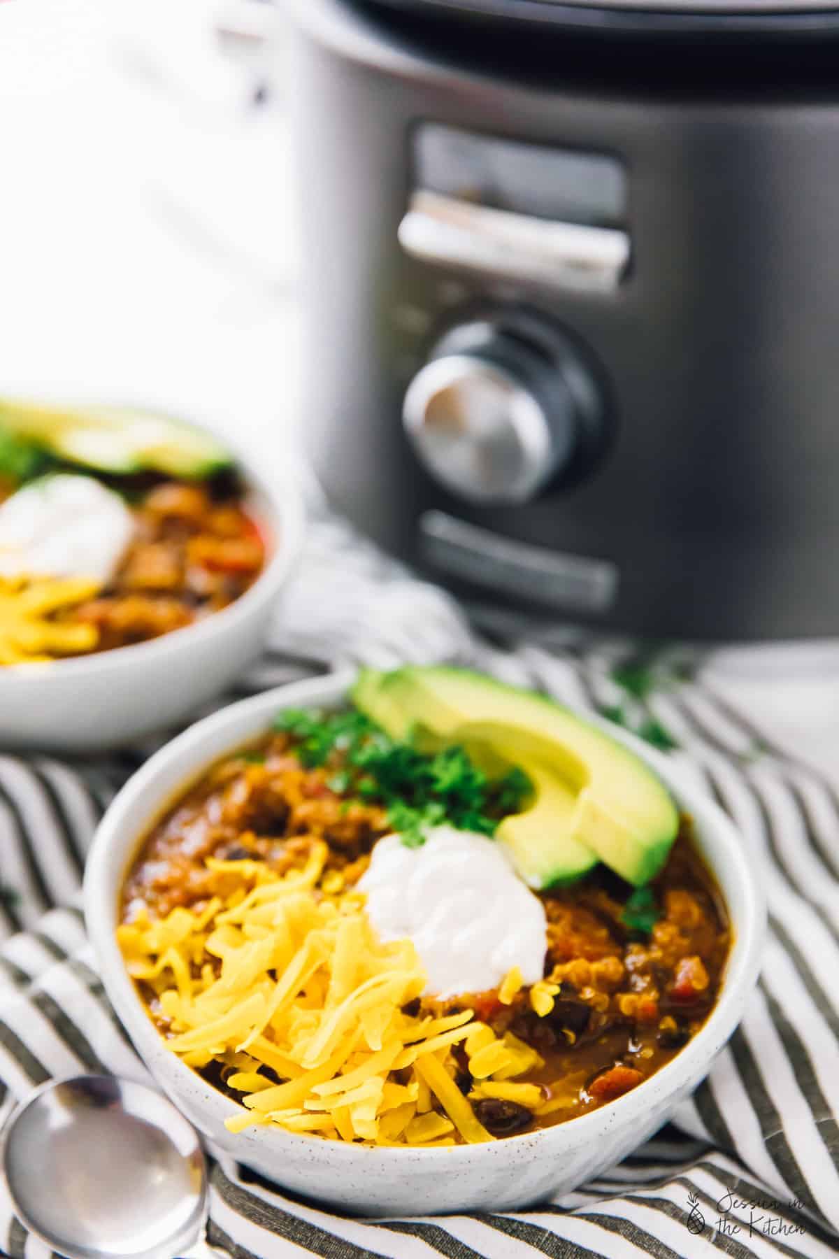 Two bowls of quinoa chili, in front of a slow cooker. 