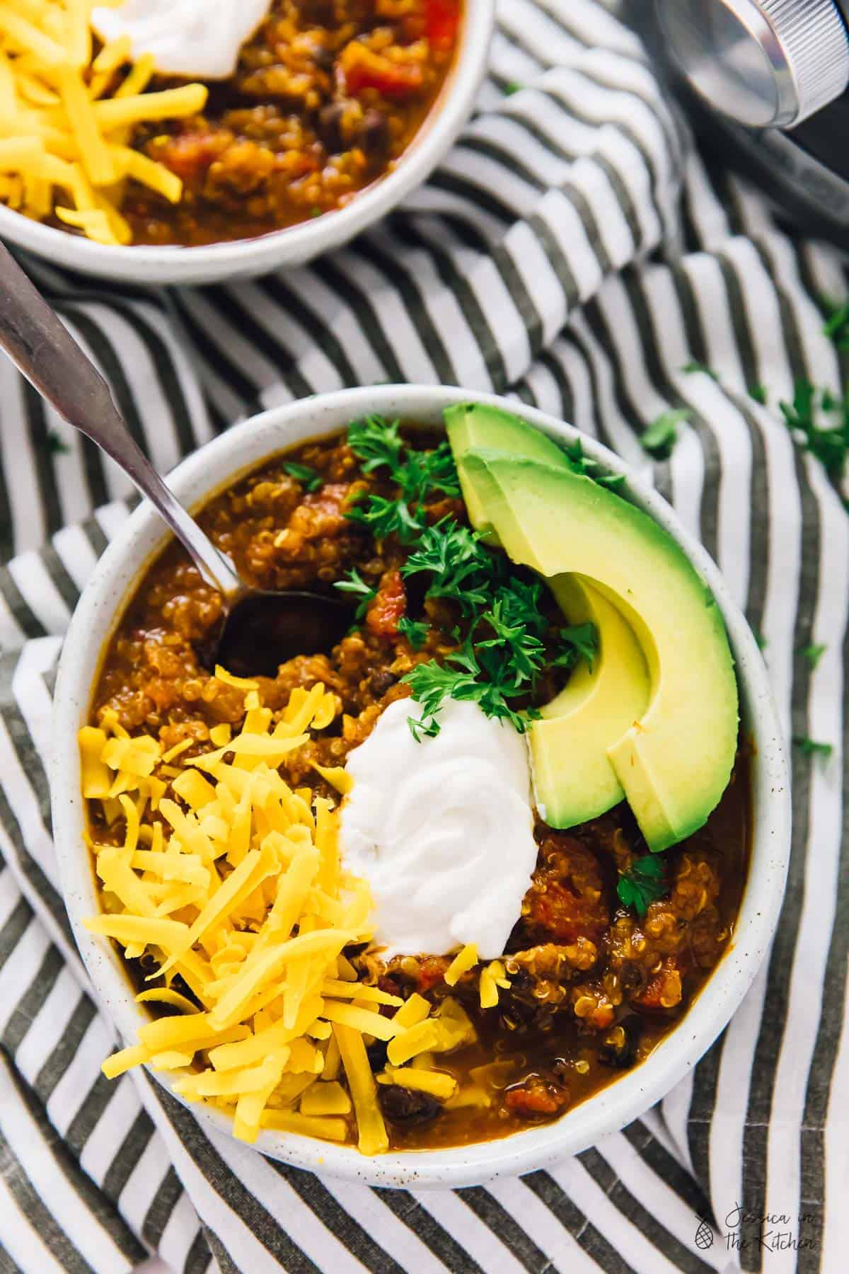 Overhead view of slow cooker pumpkin quinoa chili in white bowls, with toppings. 