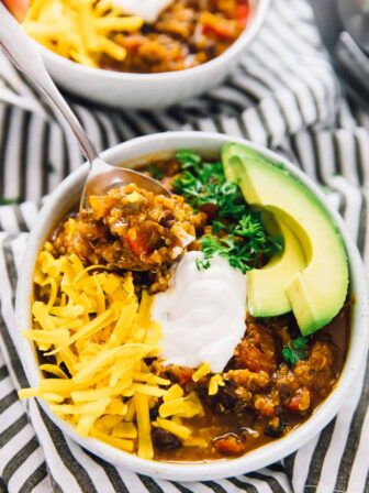 Slow cooker pumpkin quinoa chili, in white bowls, topped with avocado.