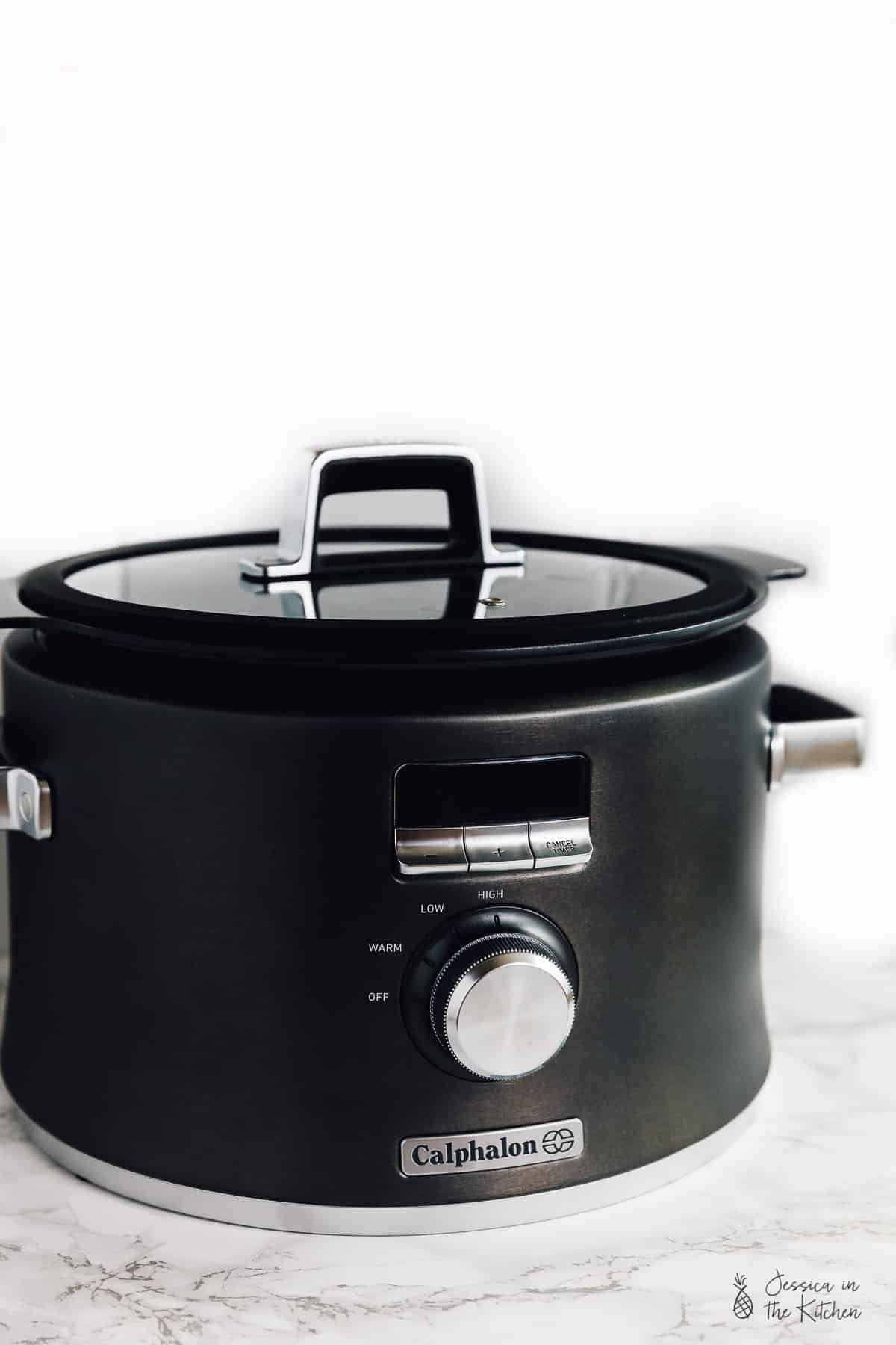 A black slow cooker on a white table top. 