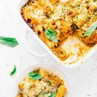 Overhead view of vegan cheese pasta bake on a white plate and in a white baking dish.