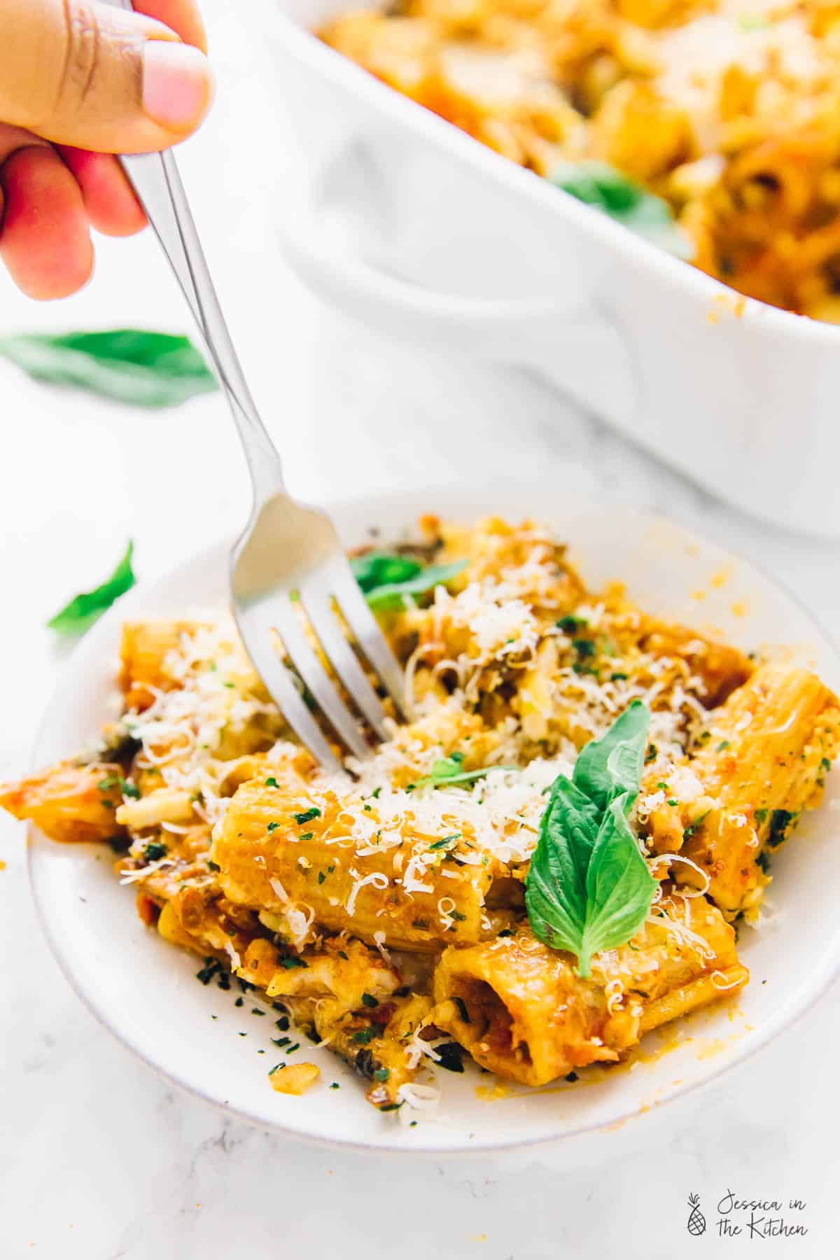A fork digging into vegan cheese pasta bake, on a plate. 