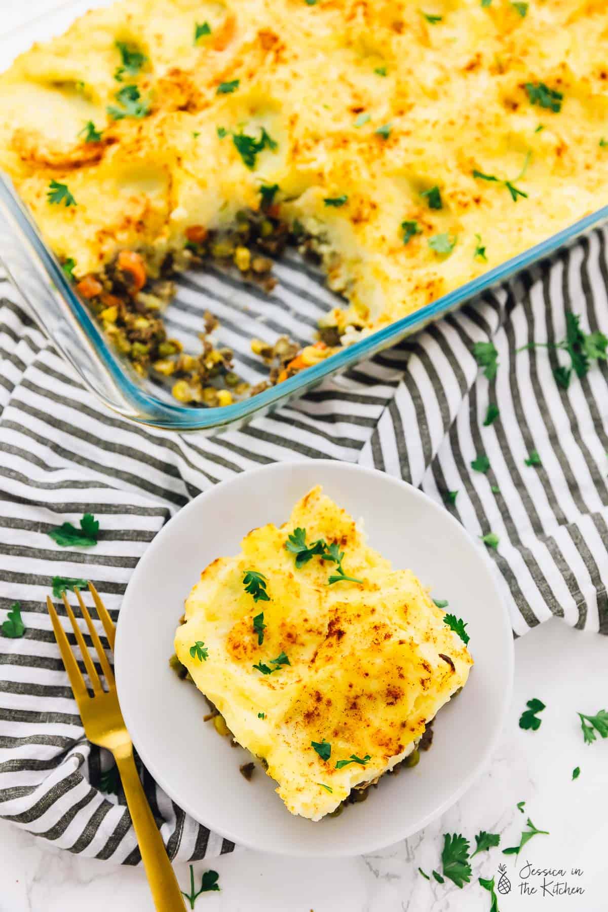 A portion of vegan shepherd's pie on a plate and in a baking dish.