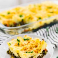 A portion of vegan shepherd's pie on a white plate with more pie in the background, in a baking dish.