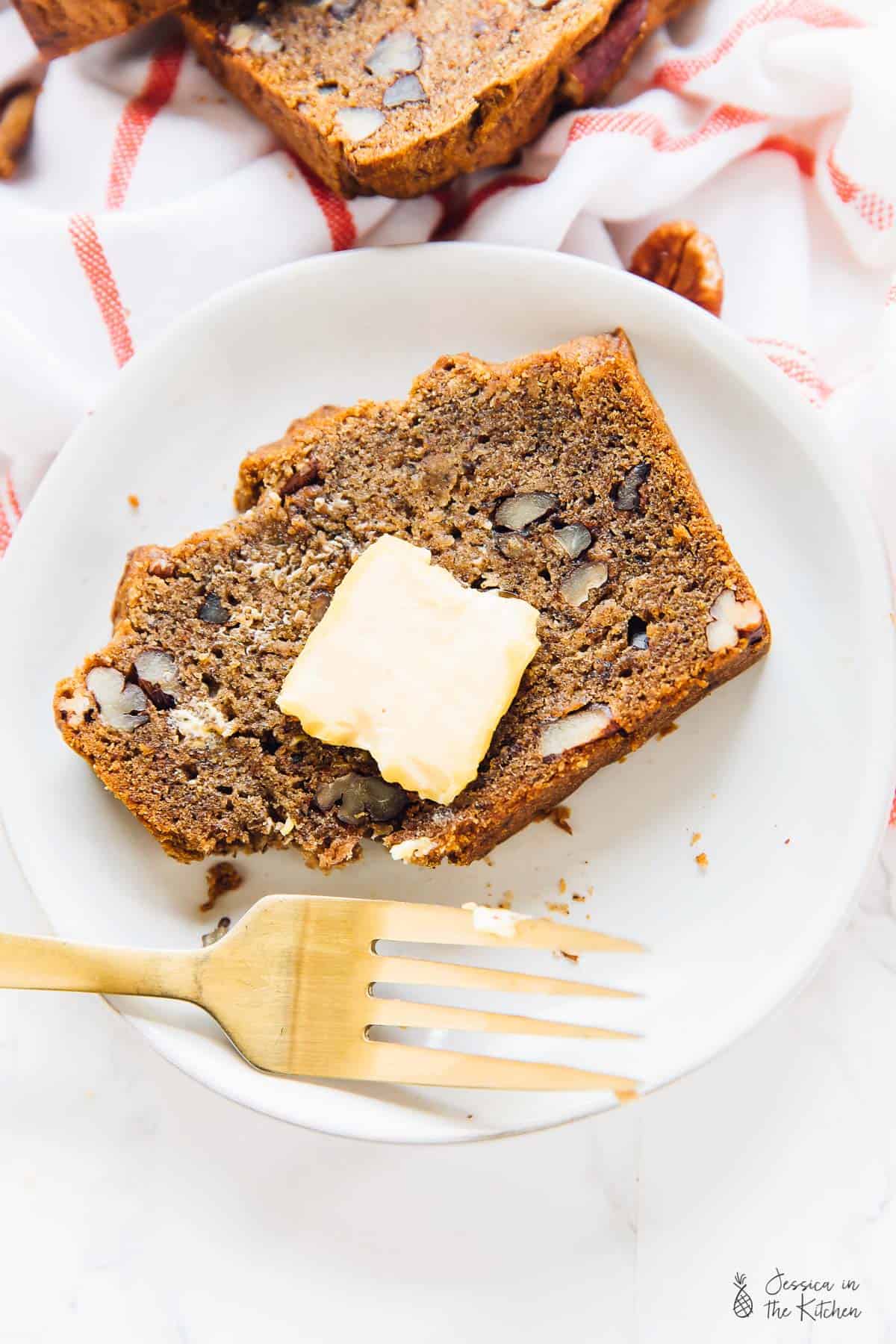 Top down view of a slice of banana bread, with a pat of butter on top. 