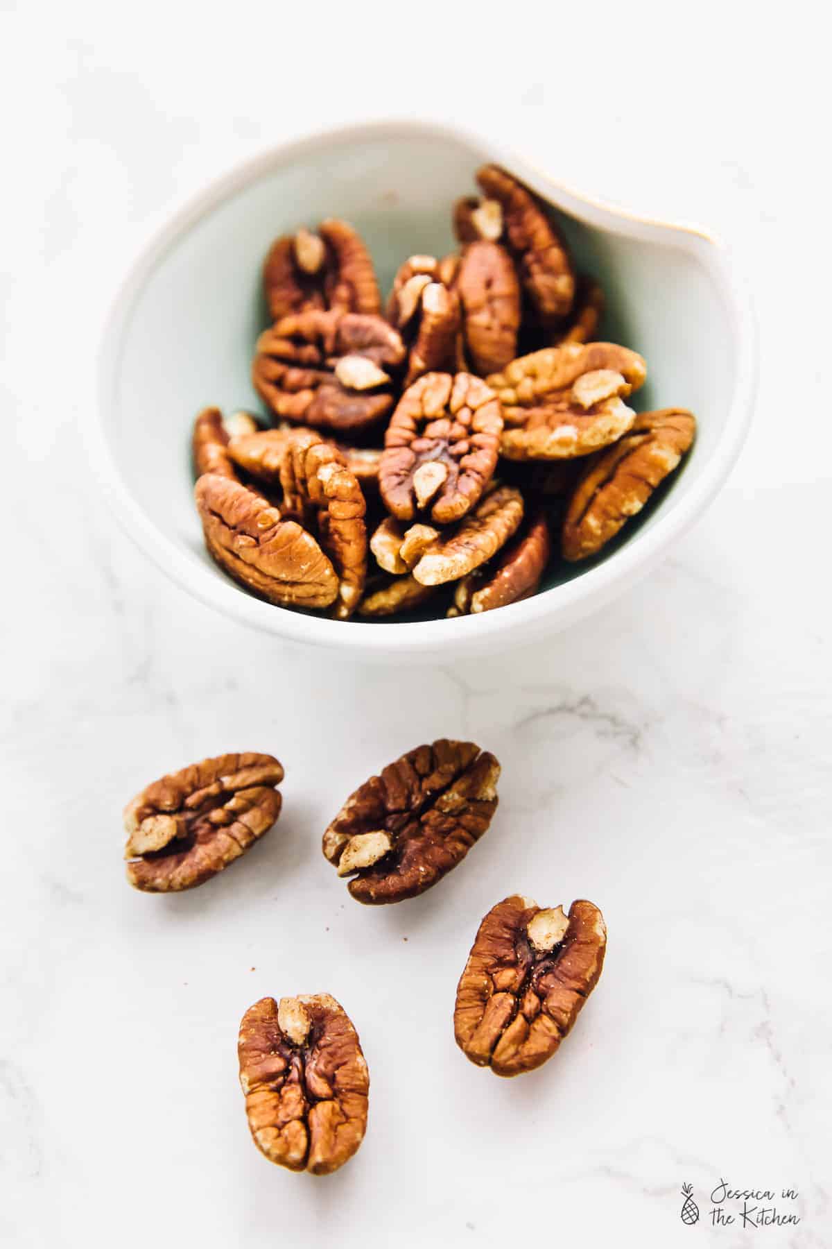 Pecans in a bowl, with loose pecans next to them.