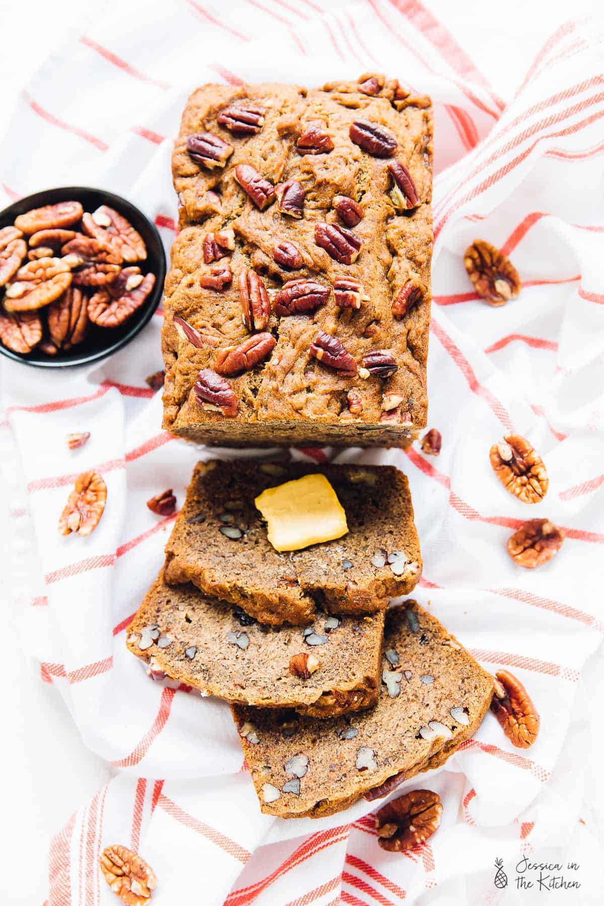 Sliced banana bread on a cloth, surrounded by pecans. 