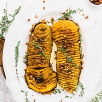 Overhead shot of hasselback butternut squash on a plate, topped with pecans.